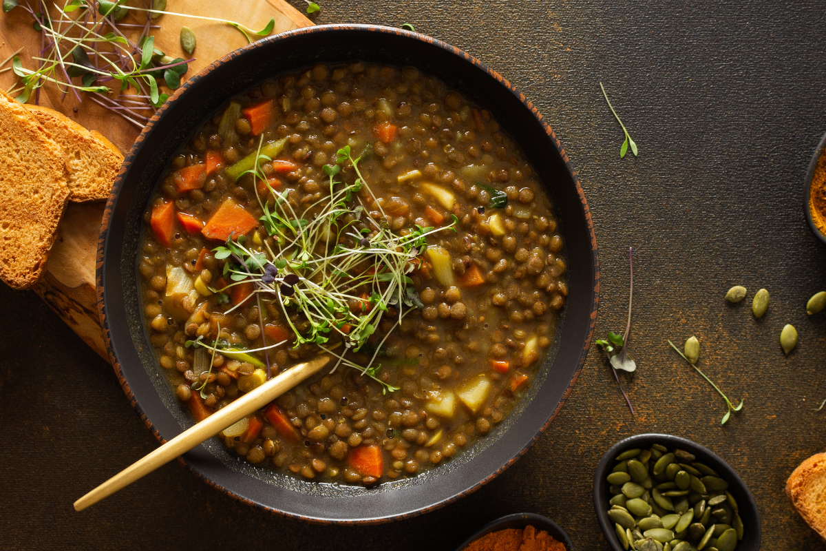 Fenugreek soup with crispy herbs with slices of bread against a dark background.