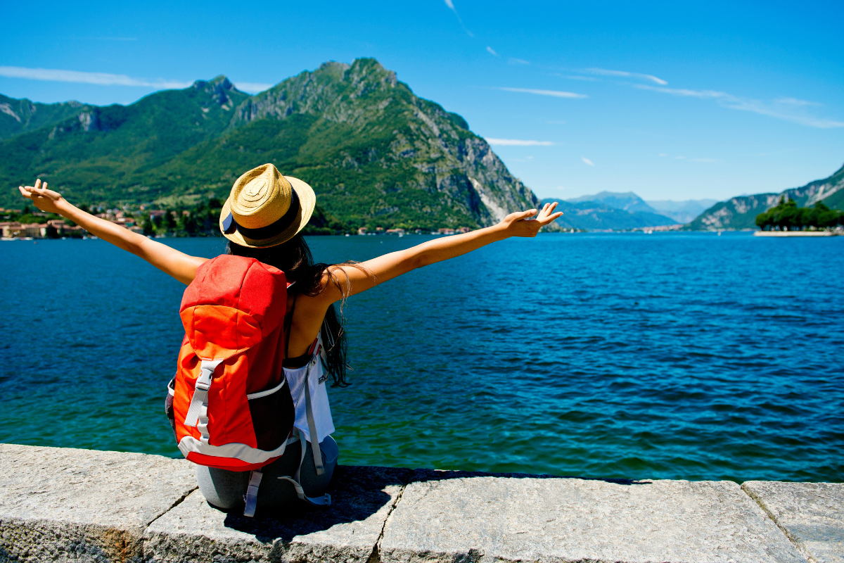 Woman with open arms and a backpack admiring a lake.