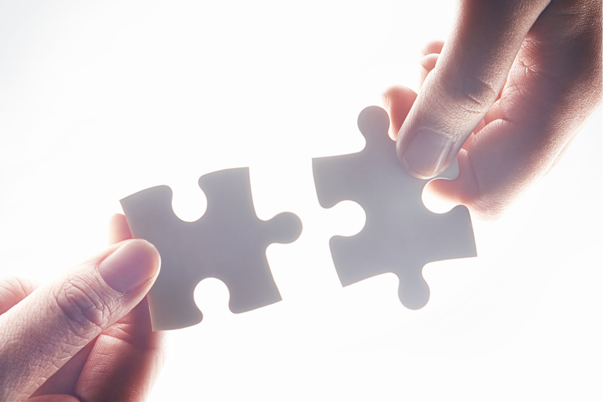 Two hands each holding a puzzle piece, about to connect them, symbolising the concept of synergy and collaboration.