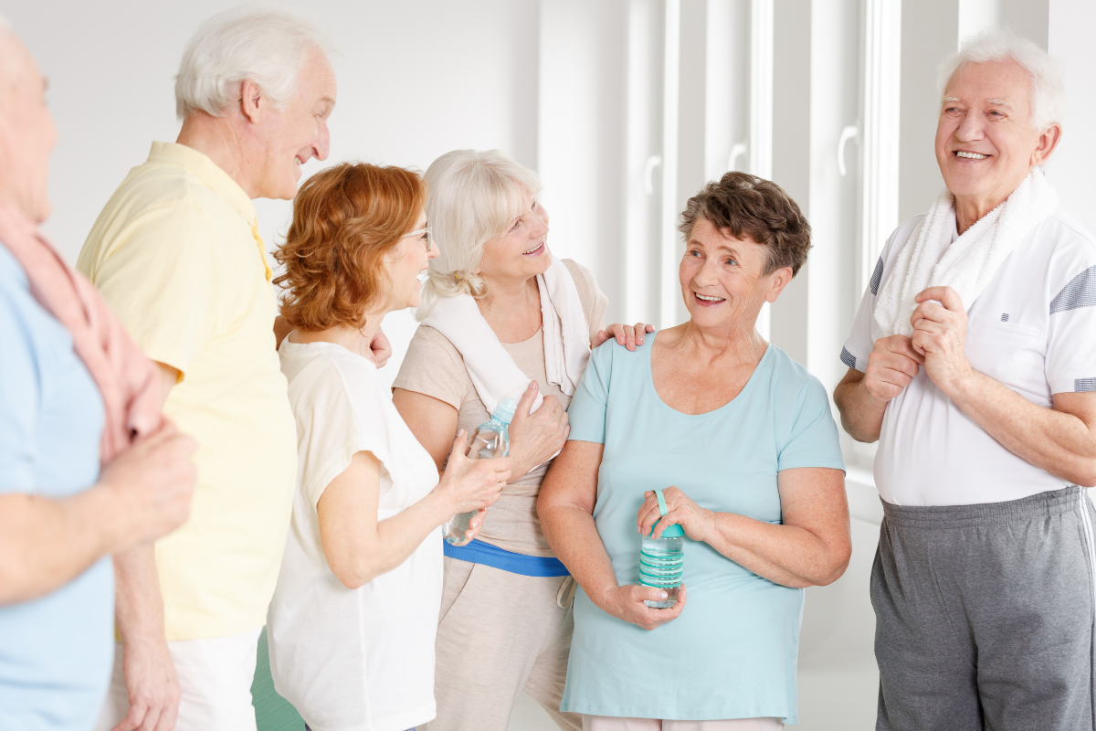 A group of happy seniors chatting and holding water bottles after a fitness class, illustrating the benefits of community and social interaction for health.