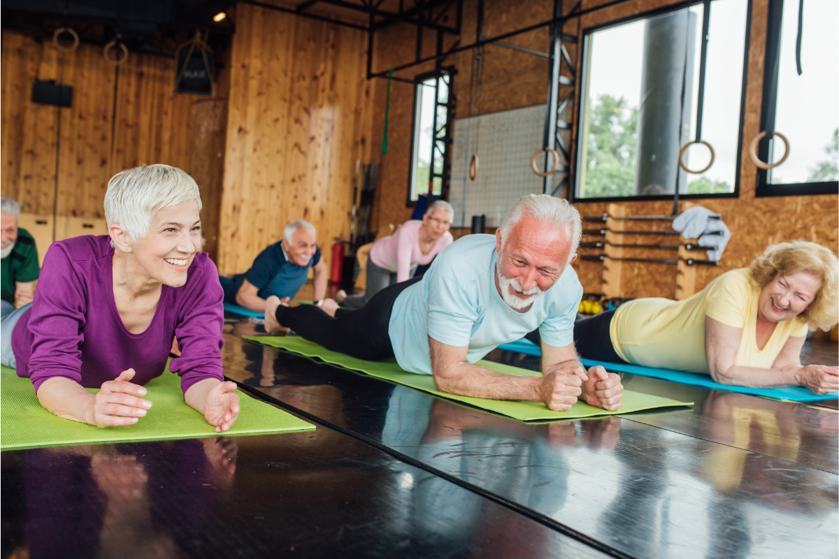 A group of smiling older people performing planks on mats.