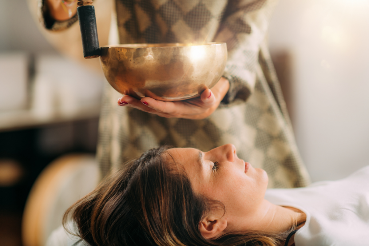 Image of a woman lying down with singing bowls being used in sound therapy session.