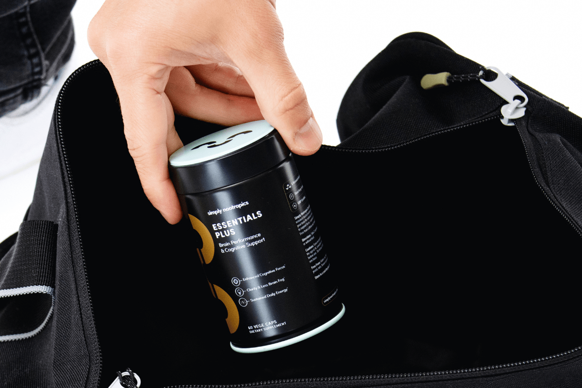 Hand placing a Simply Nootropics Essentials Plus bottle into a black gym bag.