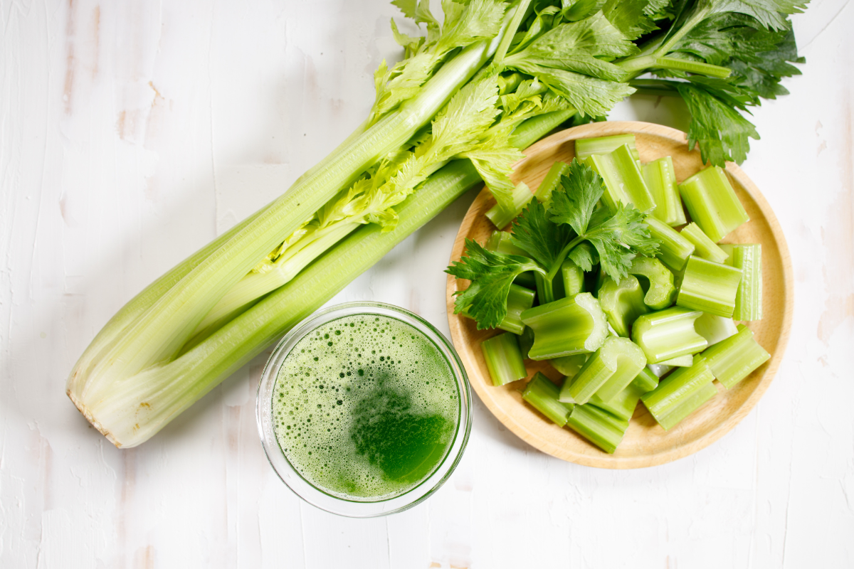 Fresh celery stalks, chopped celery, and a glass of green celery juice on a white background.