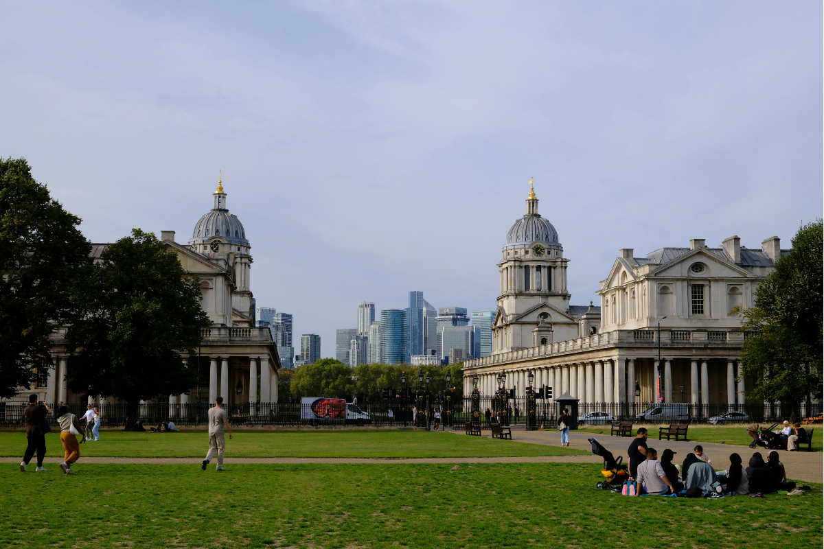 Urban park with people relaxing, historic buildings and city skyline beyond.