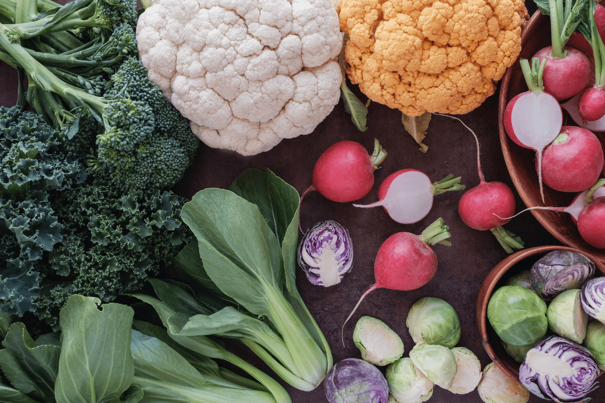 A variety of fresh vegetables including broccoli and kale displayed on a dark background.