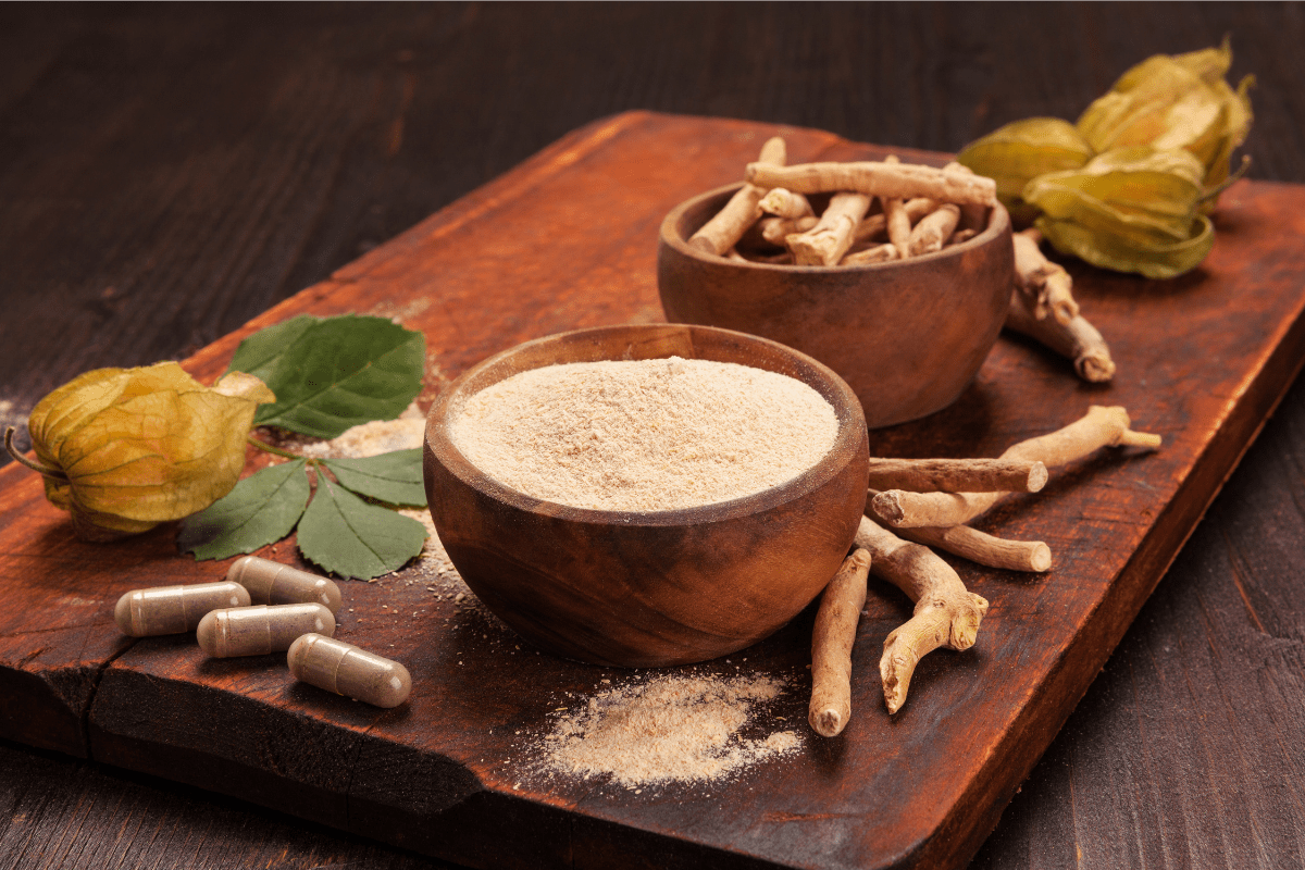 Image of Ashwagandha roots, powder, and capsules displayed on a wooden surface with natural leaves.