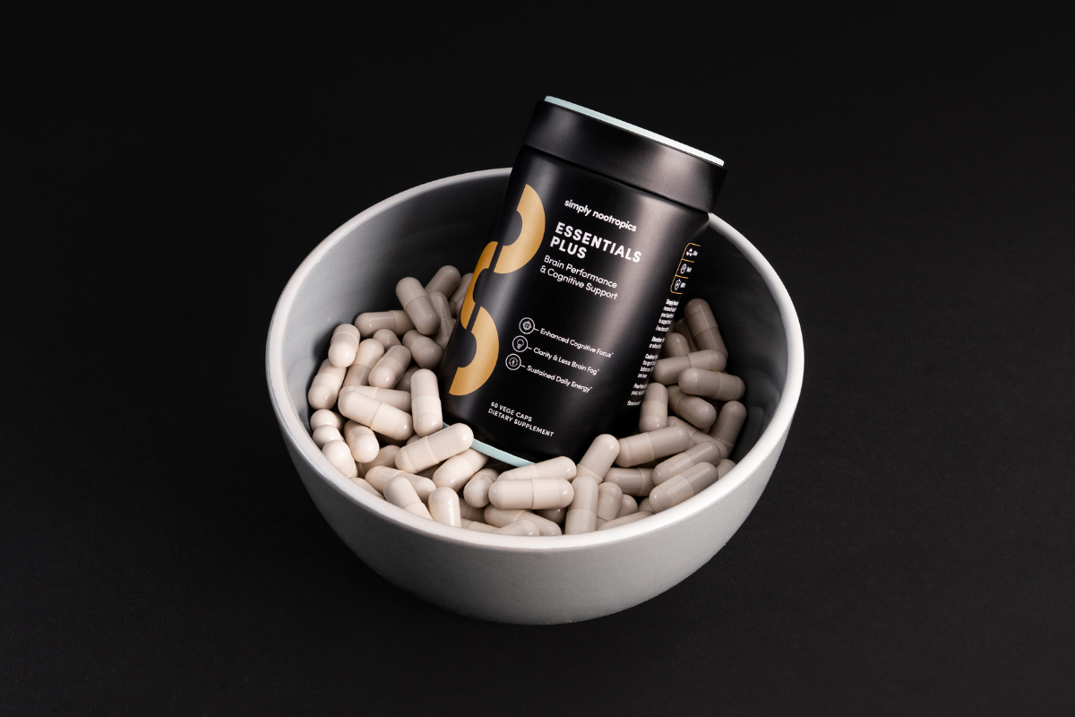 Simply Nootropics Essentials Plus bottle in bowl filled with capsules on black background.