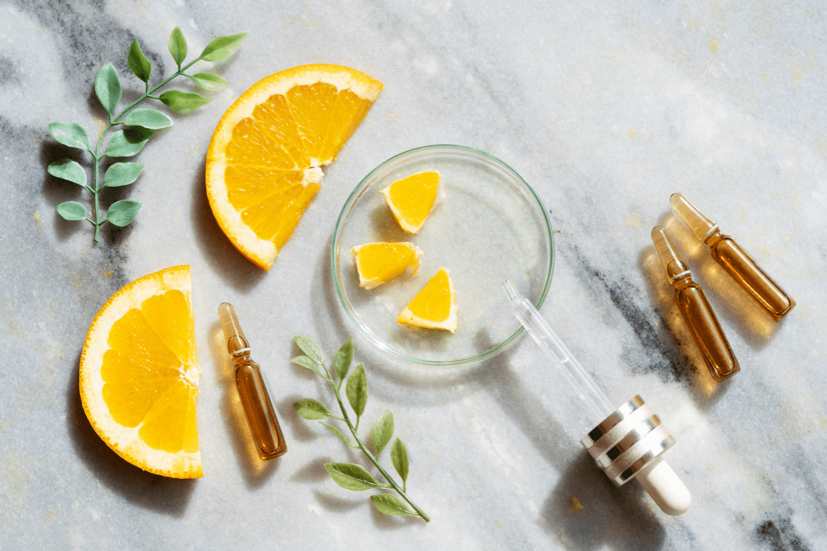 Sliced oranges, glass dropper, and serum ampoules on a marble surface, representing Vitamin C for skincare and collagen support.