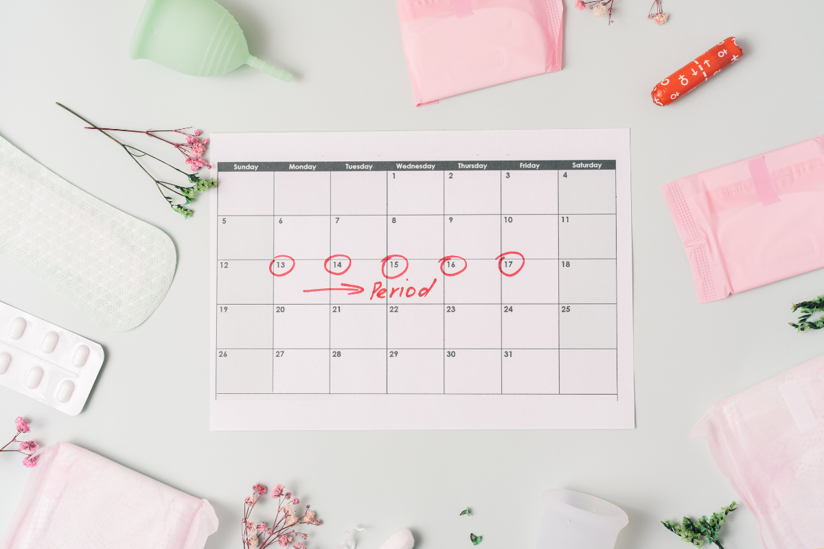 Calendar showing period dates circled in red, surrounded by pads, tampons, and a menstrual cup.