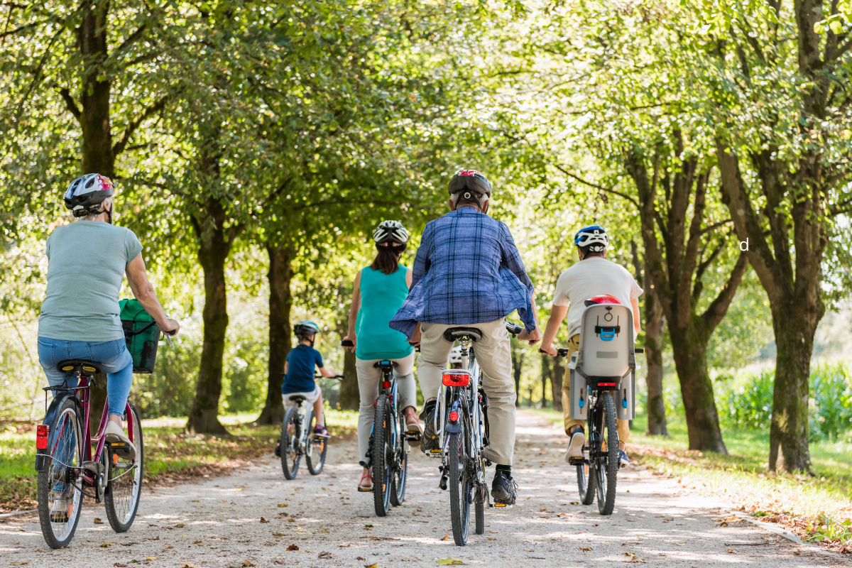Group of people of different ages cycling together along a tree-lined path.