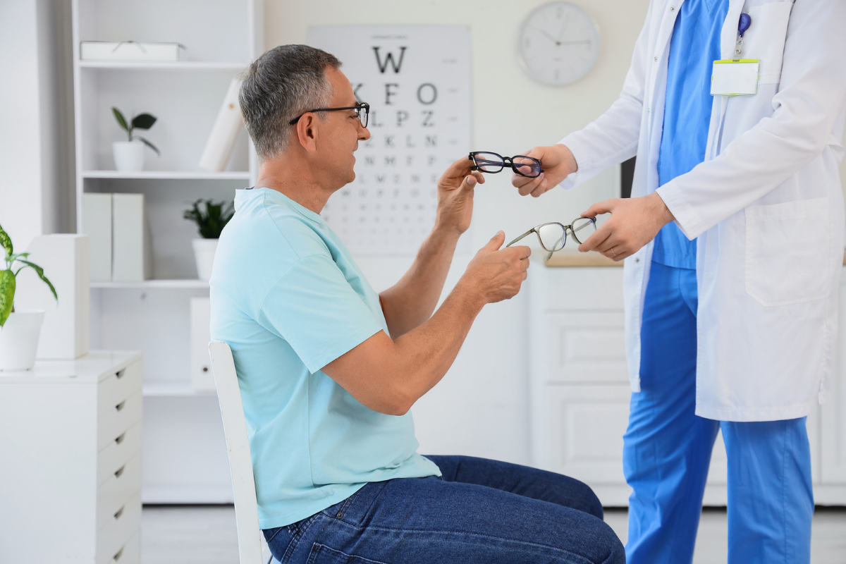 Older man choosing glasses during an eye exam with an optometrist.
