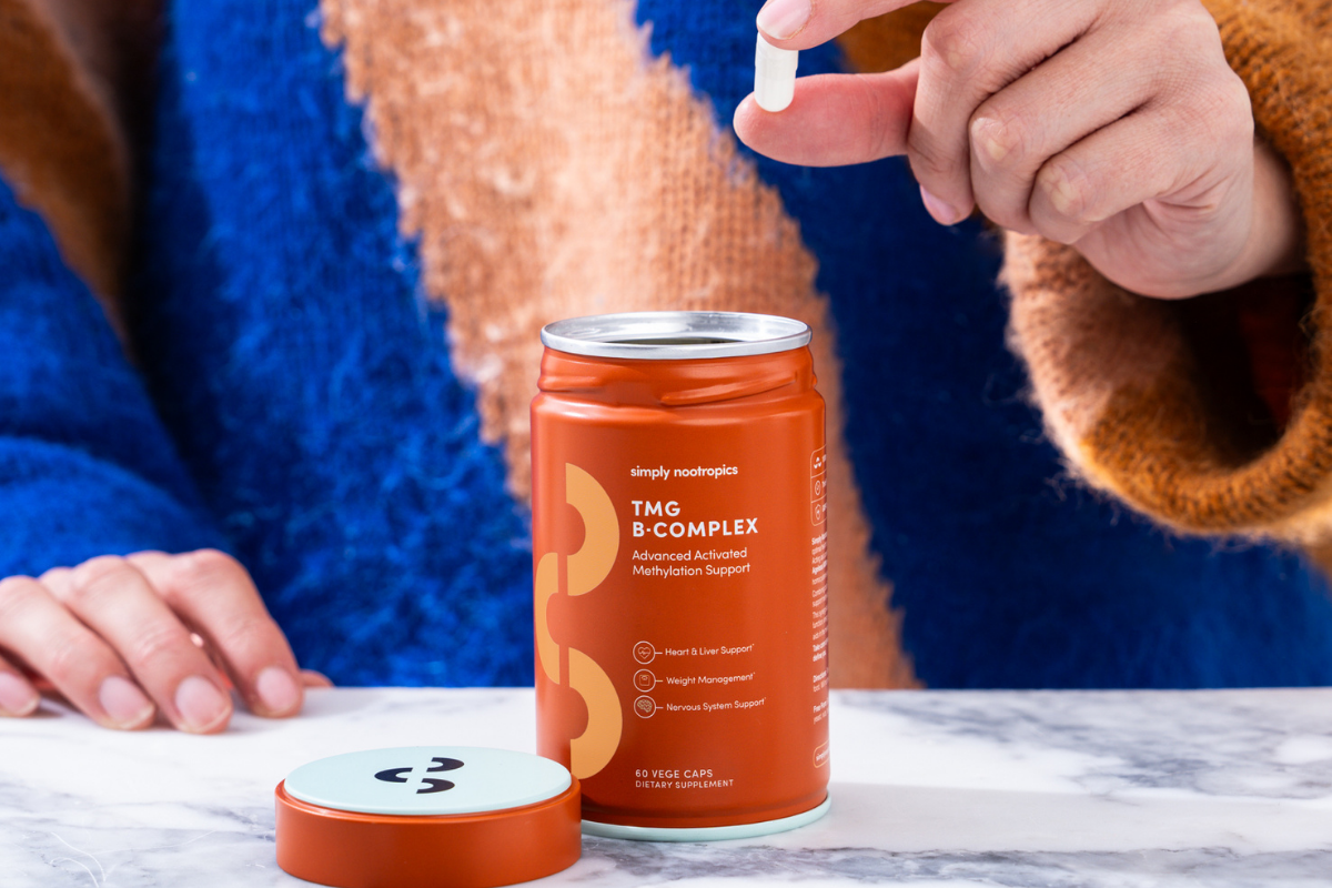 Hand holding a capsule above a Simply Nootropics TMG B-Complex container.