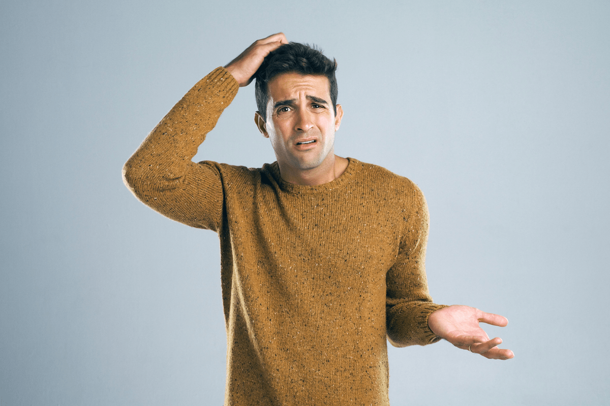 A confused man wearing a brown sweater, scratching his head with one hand and gesturing with the other, expressing uncertainty.