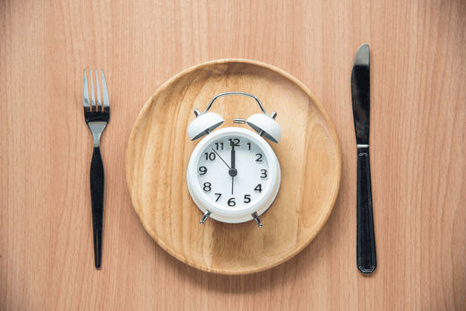 Plate with a clock in the center, surrounded by a fork and knife, symbolizing fasting and meal timing.