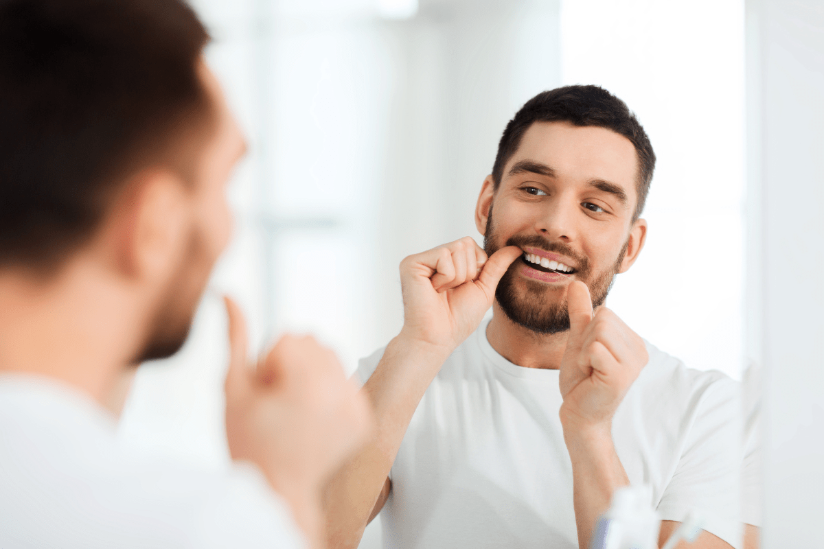 Man flossing his teeth while looking in the mirror.