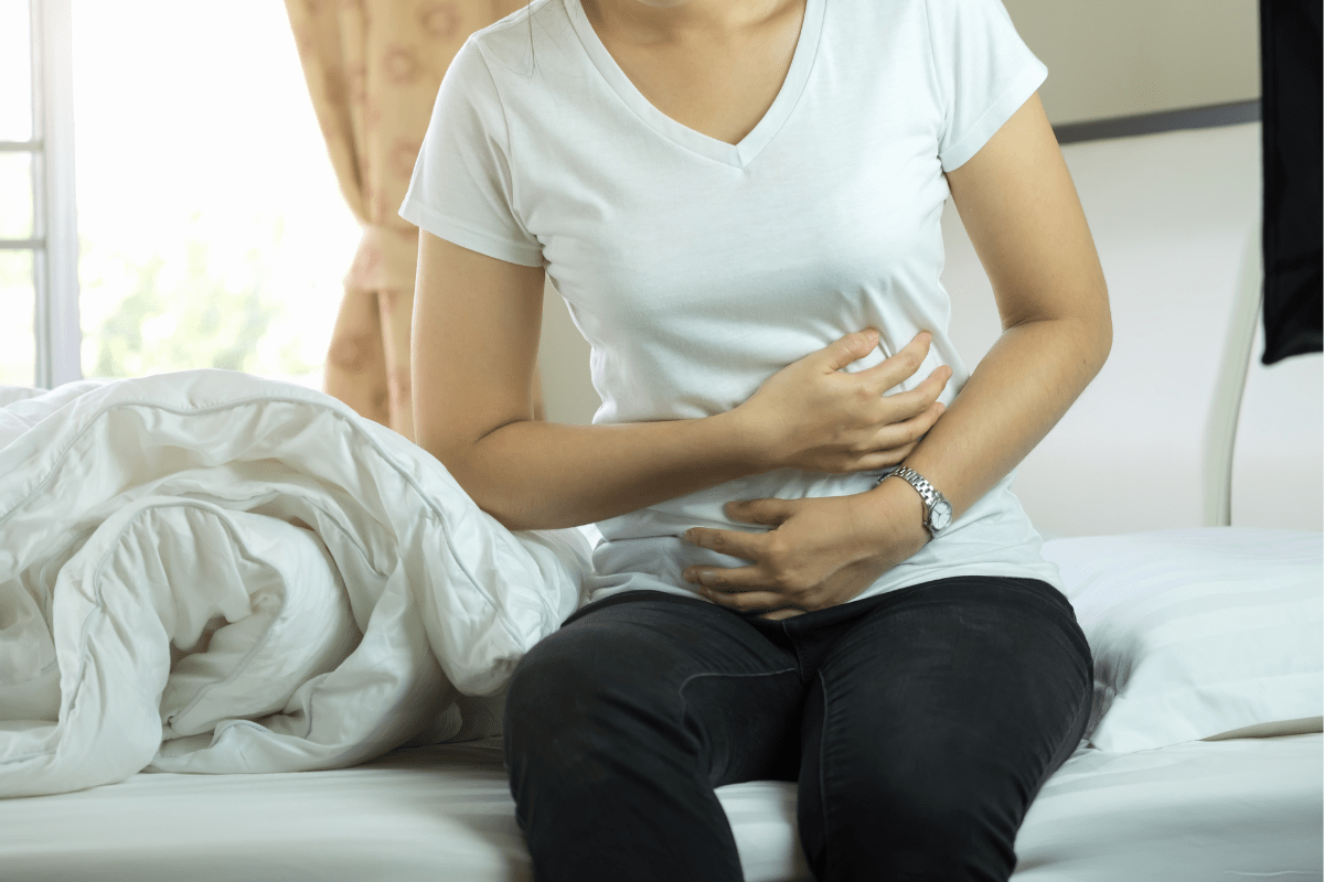 Woman sitting on bed holding her stomach in discomfort.