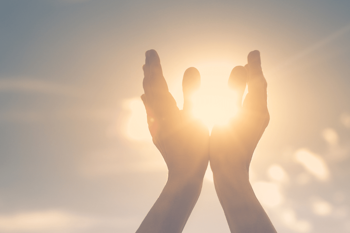 A pair of hands raised towards the sky, cupping the bright sunlight.