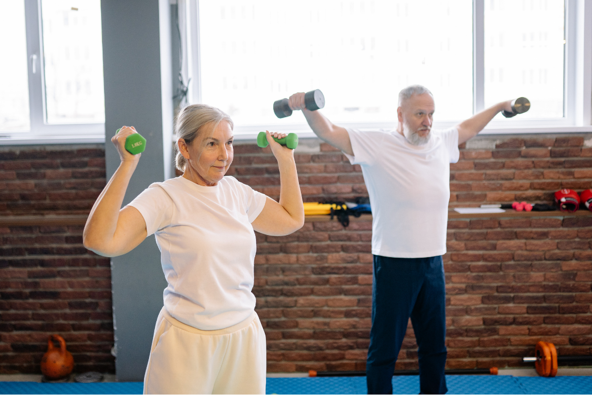 Older adults doing dumbbell exercises in a gym.