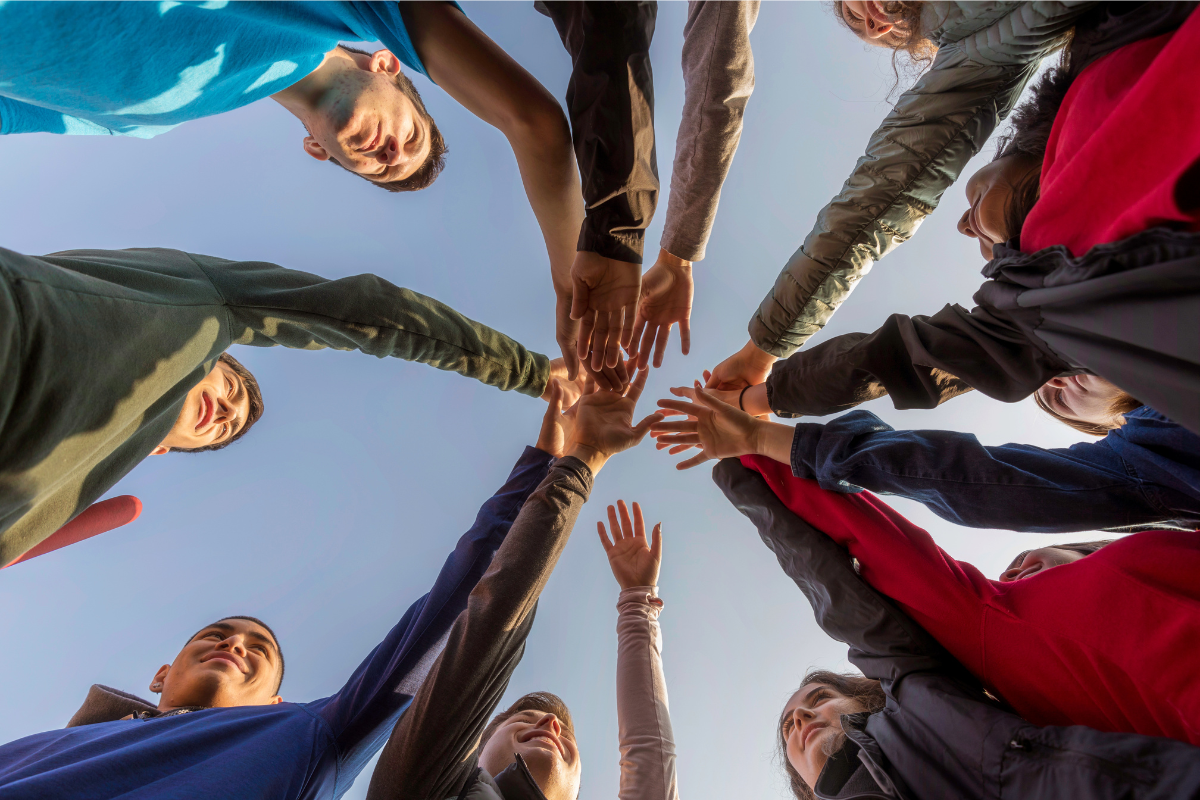 Group of diverse individuals standing in a circle, reaching their hands together in the centre.