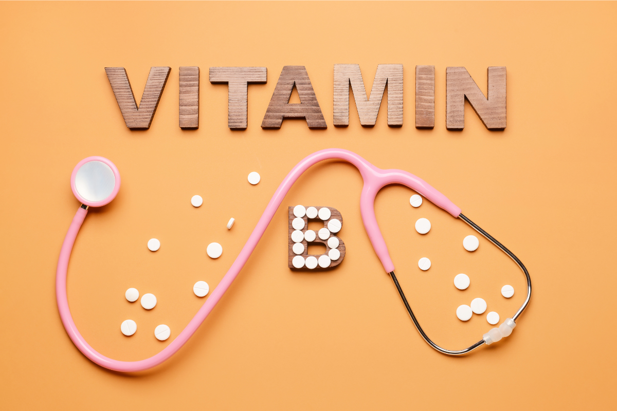 Vitamin B concept with a pink stethoscope and white tablets forming the letter 'B' on an orange background.