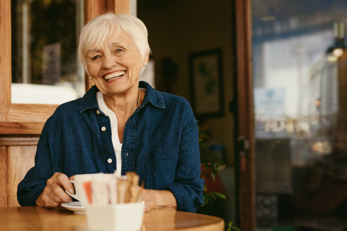 Older woman smiling over coffee at a café.