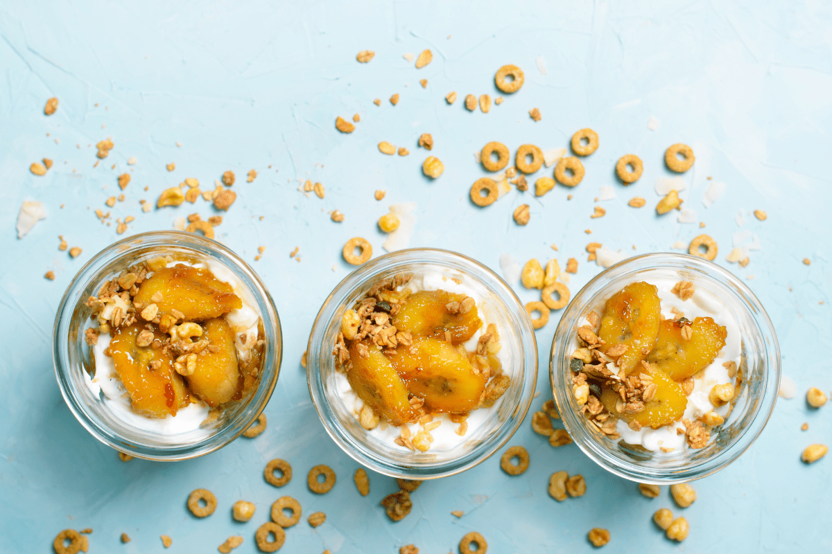 Three glass jars filled with caramelized banana, granola, and yogurt parfait.