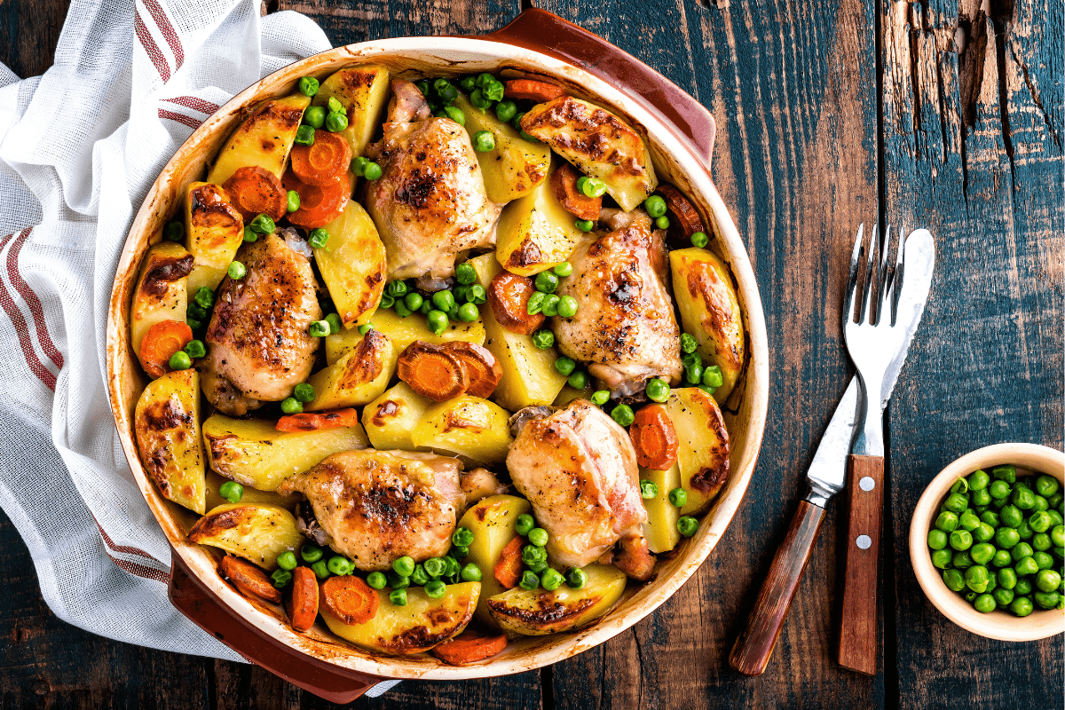 Roasted chicken thighs with peas, carrots, and potatoes in a rustic dish.