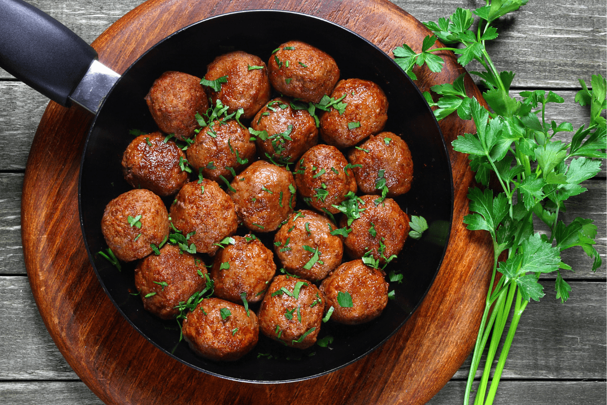 Lamb meatballs in a black pan, garnished with fresh parsley.