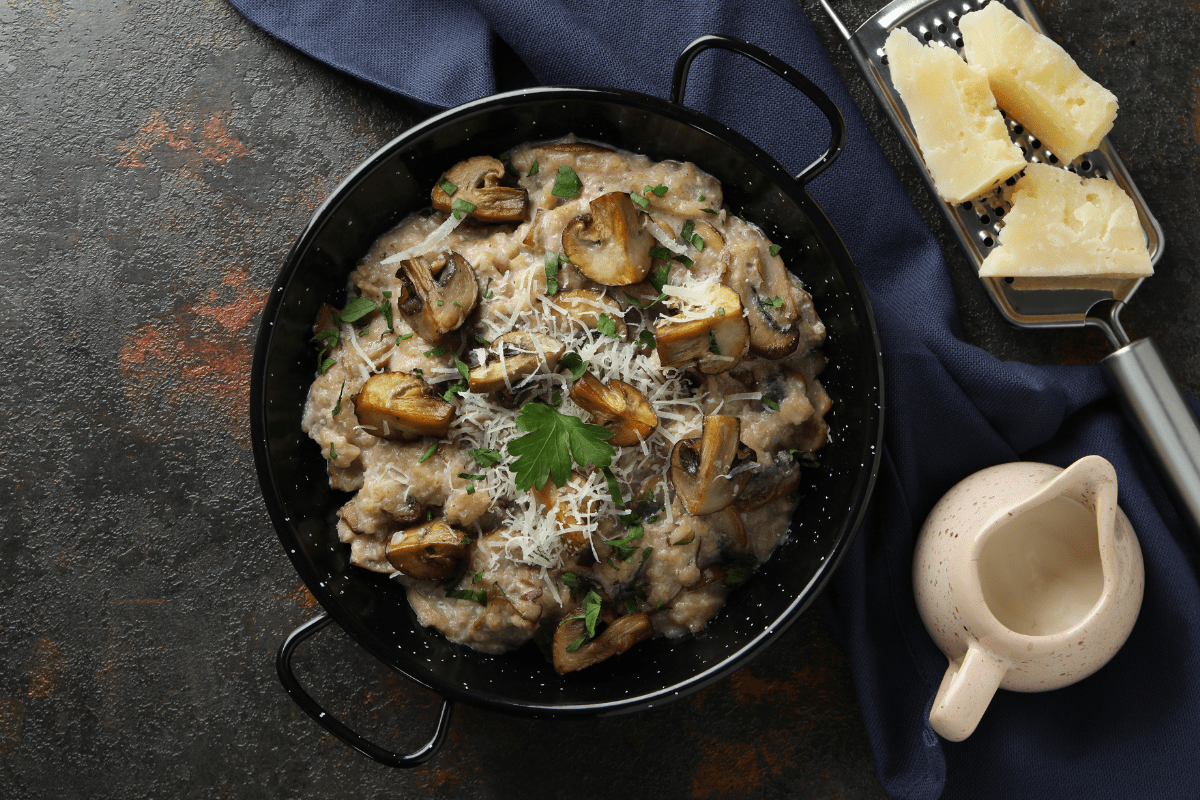 Black bowl of creamy mushroom risotto topped with sautéed mushrooms, parsley, and grated Parmesan cheese.