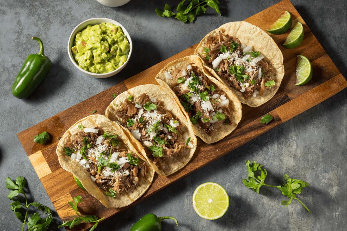 Four tacos on a wooden board.