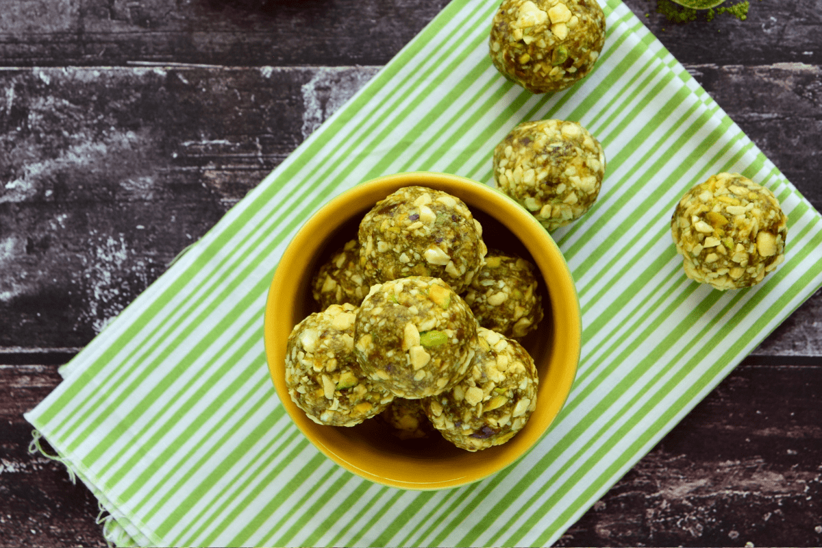 Bowl of homemade pistachio and oat bliss balls on a striped green napkin.