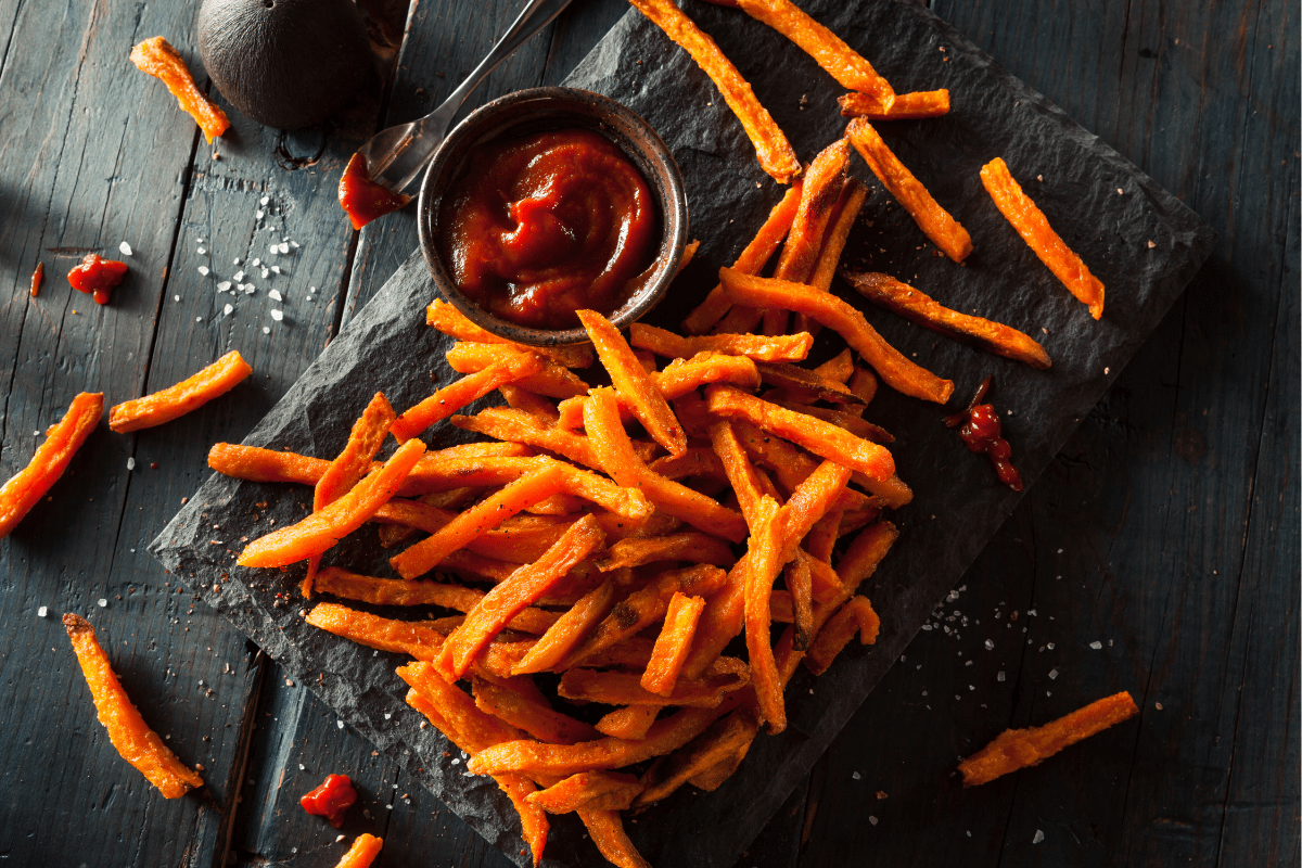 Golden crispy sweet potato fries served with a rich and spicy dipping sauce on a dark slate plate.