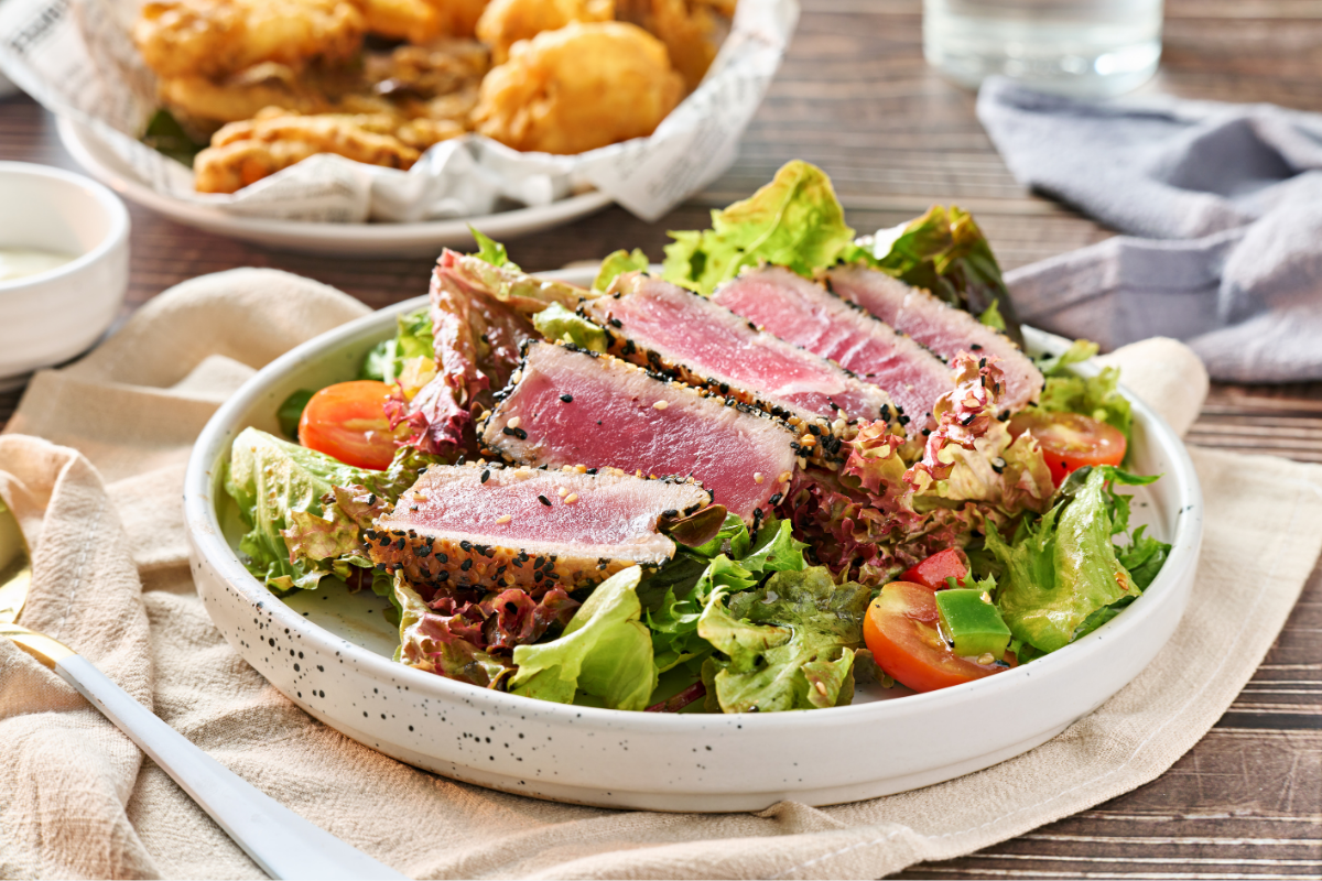 Seared tuna salad with mixed greens, avocado, and cherry tomatoes on a white plate.