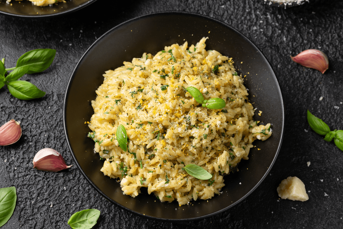 A black plate filled with lemon and garlic orzo, garnished with fresh basil and grated Parmesan.